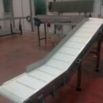 Convoyeur incliné à bande modulaire conçu pour optimiser l'accumulation et le transport de produits, comme des cartons et des bacs, tout en s’adaptant aux contraintes spécifiques des environnements industriels.