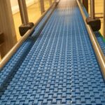 Cette image présente un convoyeur à bande modulaire, conçu pour répondre aux besoins de gestion de l'accumulation de produits tels que des cartons et des bacs, tout en s’adaptant aux spécificités de l’environnement industriel du client. Grâce à sa conception modulaire, ce convoyeur peut gérer des changements de direction (courbes) et de niveau (élévations), assurant une intégration optimale dans divers agencements industriels. En plus de sa flexibilité, ce convoyeur est fabriqué pour résister aux nettoyages fréquents à grandes eaux et aux produits désinfectants, garantissant une hygiène maximale pour des secteurs tels que l'agroalimentaire et le pharmaceutique. Ce convoyeur représente une solution idéale pour optimiser les processus de production tout en maintenant des standards élevés de propreté et de durabilité.