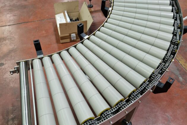 Convoyeur courbe en inox à rouleaux motorisés, idéal pour le transport efficace de produits dans une installation de production.