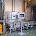 Ligne de convoyage de conteneurs IBC dans l'industrie chimique avec convoyeurs à chaînes à palettes métalliques.