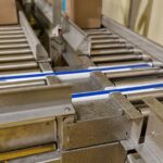 Convoyeur industriel à rouleaux intégrés avec des courroies de transfert latéral, optimisés pour la transition de cartons dans les environnements industriels.