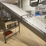 Convoyeur agroalimentaire à bande doté d'un racleur et d'un guide de produit,